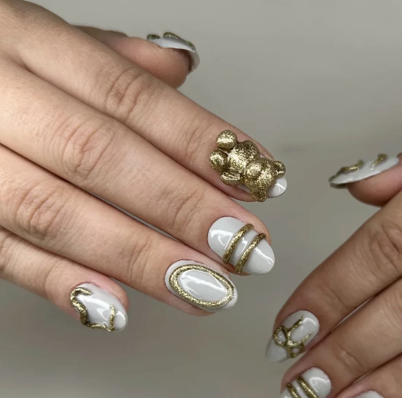 Nail art branca com detalhes dourados e urso 3D